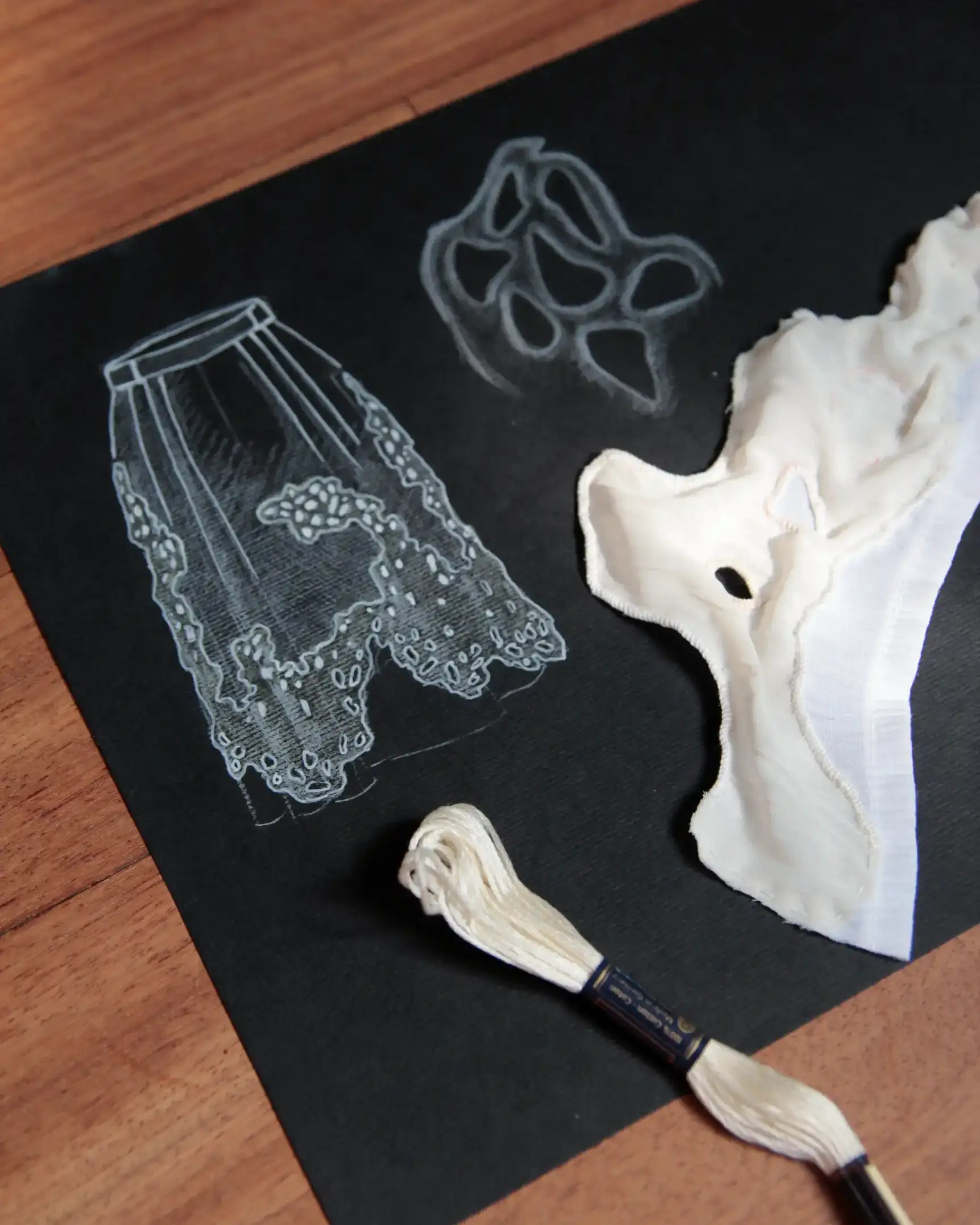 Drawing of a white skirt on black paper, whit white thread and white fabric